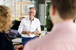 © peter scholl/Westend61 - Smiling male business professional holding digital tablet while discussing with colleagues in office