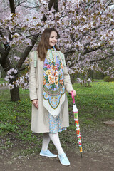 Wall Mural - Russian tourist woman in Pavlovo Posad shawl. Sakura flowering in spring garden. Landscape exhibition 