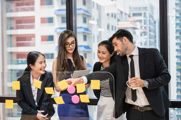 Group of multiethnic business colleagues analyzing and discussing about business plan with sticky note on board in the office