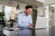 © Daniel Ingold/Westend61 - Smiling businessman using laptop at desk in office