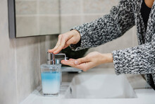 Woman Spraying Liquid Soap In Hand At Sink In Bathroom