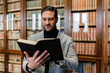 © Ezequiel Gim√©nez/Westend61 - Mid adult businessman reading book while standing in library