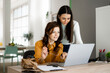 © Giorgio Fochesato/Westend61 - Smiling daughter with mother looking at laptop while sitting at desk in home office