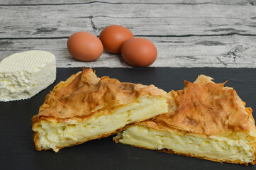 Traditional Balkan food, Serbian  gibanica with cheese (burek sa sirom), banica, Turkish borek on the plate and white cheese and eggs in the background