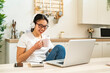 © Giorgio Fochesato/Westend61 - Young woman with coffee cup and headphones looking at camera while sitting in kitchen