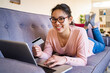 © Giorgio Fochesato/Westend61 - Smiling woman with credit card and laptop relaxing on sofa at home