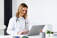 Mid adult female doctor using laptop while sitting at desk in medical clinic