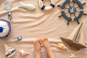 Summertime concept with ship steering wheel, decorative boats, seashells, starfishes, wooden anchor on cotton fabric background imitating sand with copy space.