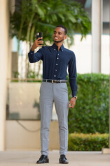 Wall Mural - African businessman outdoors at rooftop garden using mobile phone full length shot