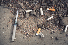 Dropped Used Syringe With Needle And Cigarettes On The Ground, Drug Addict. Threat Of Drug Addiction Concept.