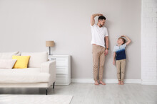 Father and son comparing their heights near wall in living room