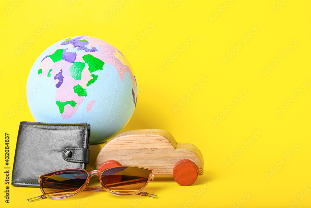Globe with wooden car, wallet and sunglasses on color background