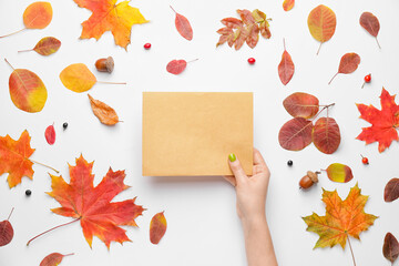 Female hand with blank card and autumn leaves on white background