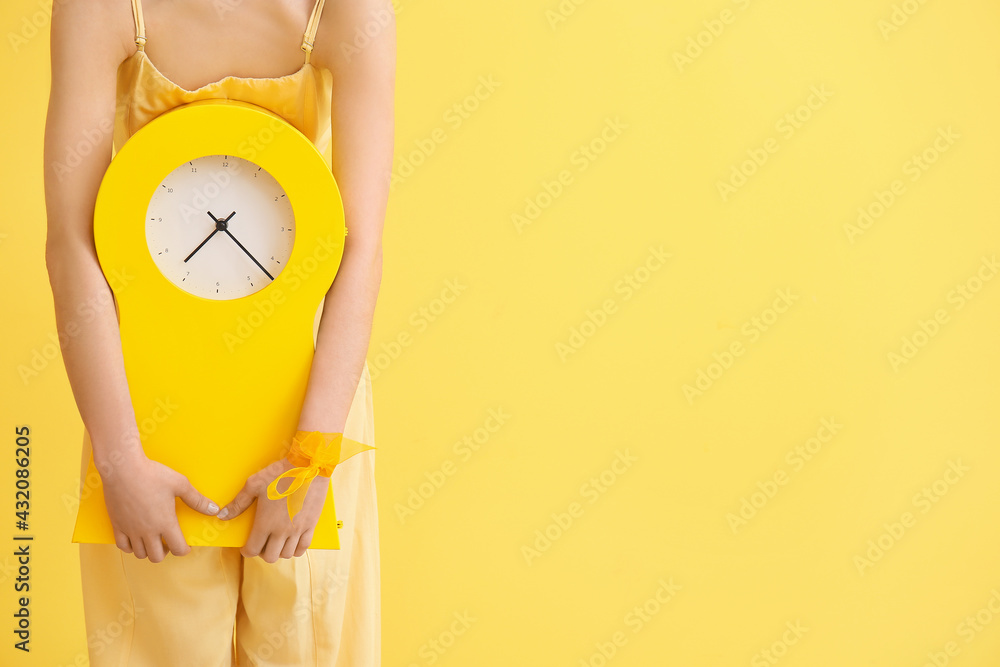Stylish young woman with clock on yellow background