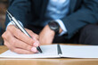© Jo Panuwat D - Businessman in suit writing something on notebook in office or cafe, hand of man holding pen with signature on paper report. business concepts