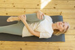 © Nata Bene - Gymnastics morning routine. Energetic senior woman doing stretching warming up exercises while lying on yoga mat on floor at home, full length. Elderly woman following healthy lifestyle on retirement