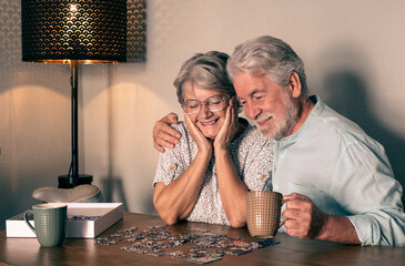 Happy senior couple at home spend time together doing a puzzle on the wooden table.