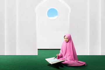 Asian Muslim woman in a veil sitting and reading the Quran