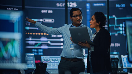 Fototapete - In the System Control Room Project Manager and IT Technical Engineer with Laptop Have Discussion, surrounded by Multiple Monitors with Graphics. Big Monitor Shows Interactive Server Blockchain Info.