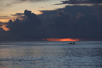 A picturesque sunset on the sea with the silhouette of a floating boat with two people in the distance on the horizon against the background of a red glow.The concept of sports and recreation