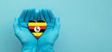 Fototapeta Natura - Doctors hands wearing surgical gloves holding Uganda flag heart