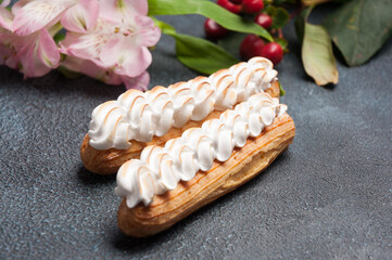 Wall Mural - Eclair with singed protein cream on a dark background decorated with flowers. Close up