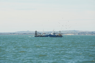 Two fishing boat, trawlers fishing Razor fish in an open Irish sea. Food industry, traditional craft, environmental damage concepts.