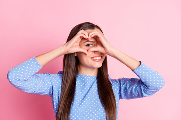 Poster - Photo portrait of playful girl looking inside heart showing with fingers smiling long straight hair isolated on pink pastel color background