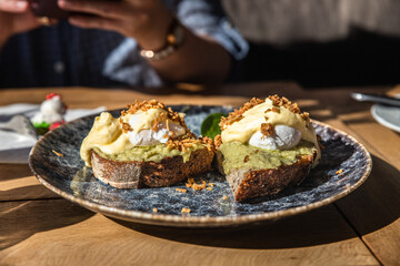 two pieces of toasted whole rye bread with mashed avocado, poached eggs and sauce. sandwiches with e