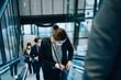 © Maskot - Female entrepreneur peeking in sling bag while standing on escalator during pandemic