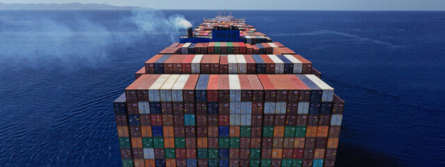 Aerial drone ultra wide photo above huge colourful container carrier vessel cruising deep blue open ocean sea