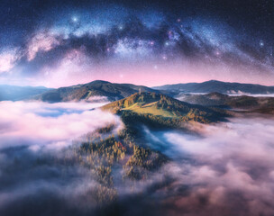 Wall Mural - milky way arch and mountains in low clouds at starry night in summer. landscape with pink sky with s