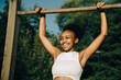 © Maskot - Smiling sportswoman hanging on monkey bar in park during sunny day