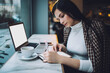 © BullRun - Serious young woman taking notes while working in cafe