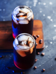 Two stylish glasses of cold brew coffee. Colored blue light. On a wooden board , black background