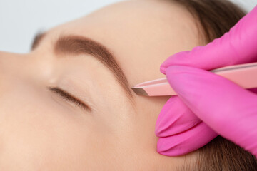 Makeup artist combs  and plucks eyebrows after dyeing in a beauty salon.Professional makeup and cosmetology skin care.