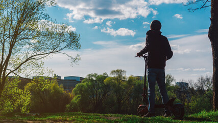 Wall Mural - A guy rides an electric scooter in a park or forest. Modern eco-friendly transport. Powerful e-scooter