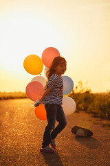 Wall Mural - Cute happy little girl playing with colorful balloons at sunset. Selective focus