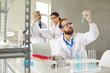© Studio Romantic - Focus on male scientist front of laptop holding test tube flask conducting chemical experiment at laboratory with senior professor and young female assistant on background. Science and research