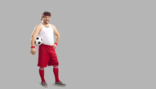 Happy Fat Man Holding Soccer Ball Under Arm. Full Body Funny Smiling Chubby Male Football Player In Headband, White Tank And Red Shorts Standing Akimbo On Free Empty Copyspace Advertising Background