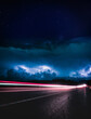 Red highway lights of the car motion with stormy clouds above at night