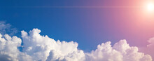 Blue Sky Background With White Puffy Clouds On A Bottom Foreground. Panorama With Fluffy Clouds And Sun Flares. Banner, Copy Space, Blank Space For Text