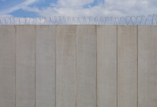 High Retaining Concrete Wall With Metal Barbed Wire Under A Cloudy Sky