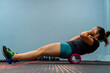 a young latina woman in the gym stretching her muscles with a foam roller.