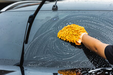 The young man washed his car with foamy cleansing foam. He was wearing gloves for washing the car. He wiped the windshield of the car.