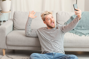 Wall Mural - Young man with mobile phone taking selfie at home