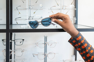 Hand of  Dark skinned woman choosing the glasses in optics store, eyesight and vision concept 