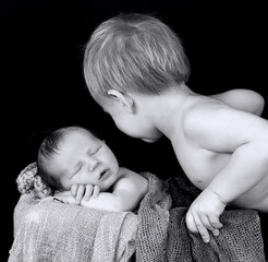 Canvas Print - Grayscale shot of a little Caucasian boy with his newborn baby brother on a basket