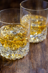 Top view of two glasses with whiskey with ice on dark wooden table, vertical, with copy space