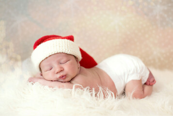 adorable newborn caucasian baby boy in a santa hat sleeping on a white fur cloth